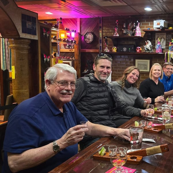 Five smiling people enjoying a tequila tasting at a long wooden table in Casa Juarez Mexican Town.