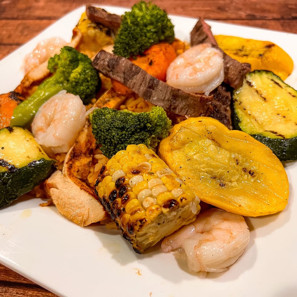 Grilled shrimp, steak, chicken, corn, zucchini, yellow squash, and broccoli on a white plate.
