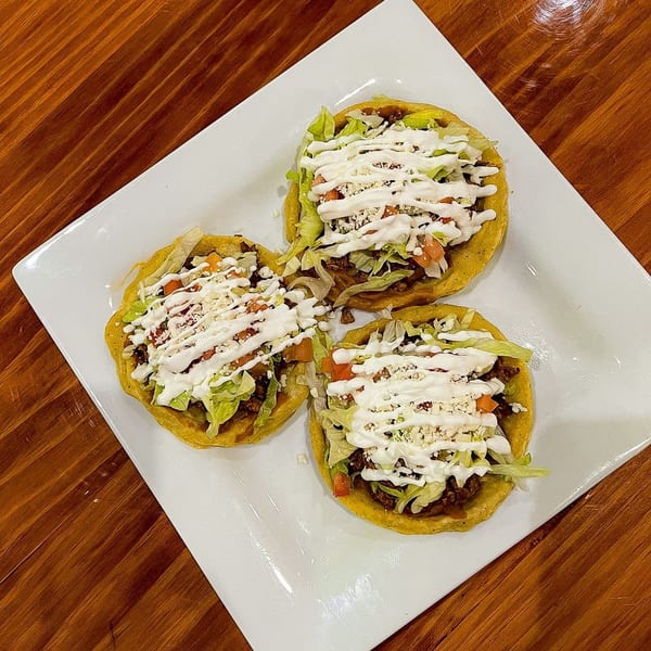 Three Casa Juarez sopes with meat, lettuce, tomatoes, cheese, and crema on a white plate.