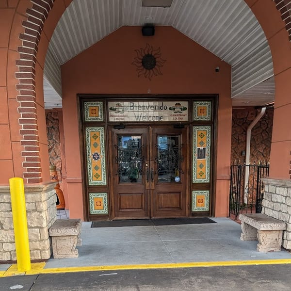 Casa Juarez Mexican Town's entrance with "Bienvenido Welcome" sign, ornate wooden doors, and decorative tiles.