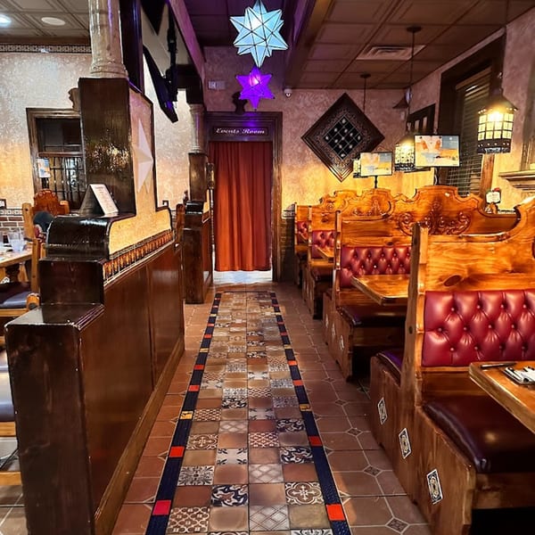 A long, narrow dining room at Casa Juarez Mexican Town with wooden booths, red cushions, and patterned floor tiles.