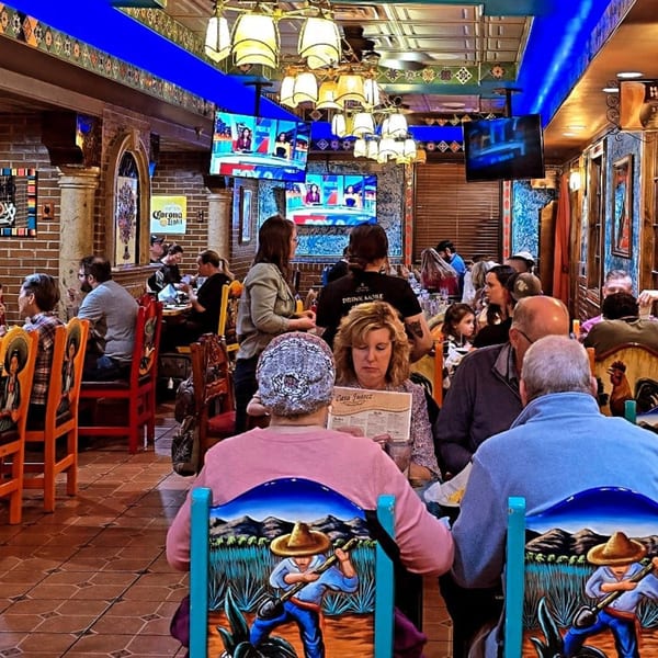 Diners seated at tables in a vibrant Casa Juarez Mexican restaurant with colorful decor and TVs.