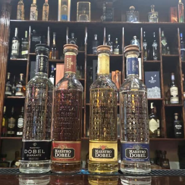 Four bottles of Maestro Dobel tequila, including Diamante, Reposado, and Blanco, on a bar shelf.