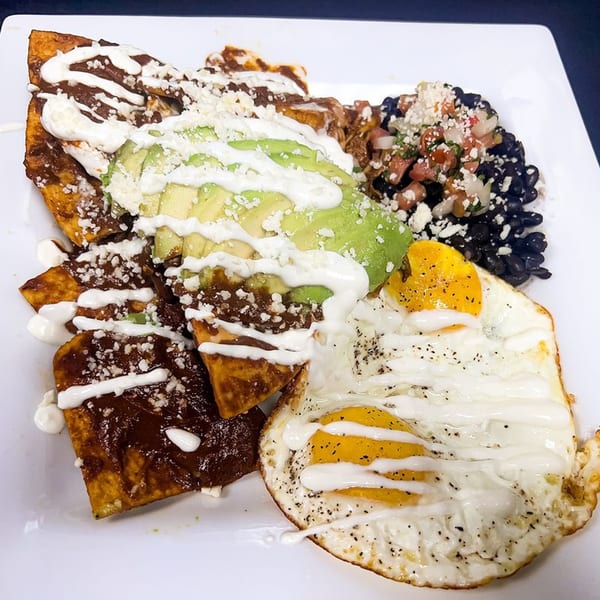 Chilaquiles with mole sauce, avocado, sour cream, cheese, black beans, and two fried eggs.