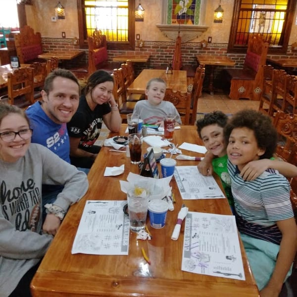 A family of six smiling at the camera while seated at a wooden table in Casa Juarez Mexican Town.