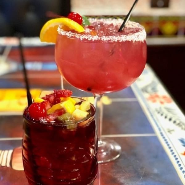 Two vibrant Mexican drinks, one a red margarita with a salted rim, the other a fruit-filled sangria.
