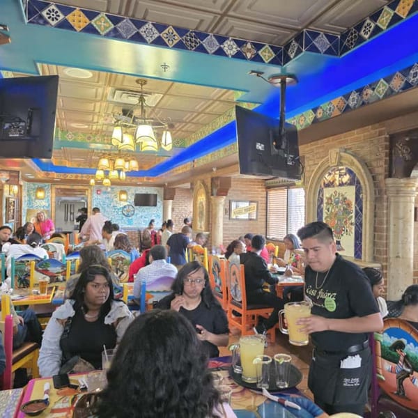 A busy dining room at Casa Juarez Mexican Town, with a waiter serving margaritas.
