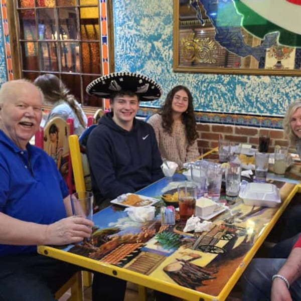 A family enjoying a meal at Casa Juarez Mexican Town, with one person wearing a sombrero.