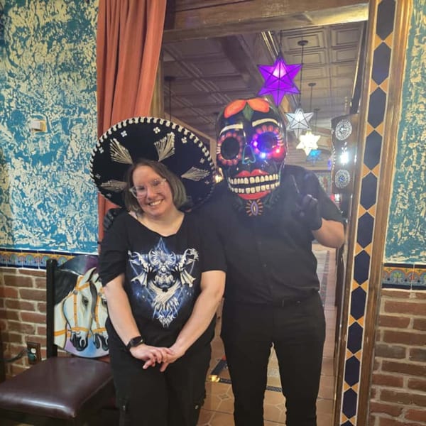 A woman in a sombrero and a person in a Day of the Dead mask pose in a Mexican restaurant.