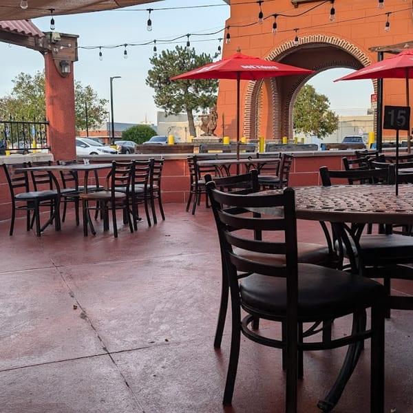 Outdoor patio at Casa Juarez Mexican Town with tables, chairs, red umbrellas, and string lights.
